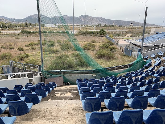 Het softbalstadion van de Olympische Zomerspelen in Athene (2004) ligt er verlaten bij. Evanonthegc, Abandoned Olympic Softball Stadium (2018). Bron: Wikimedia Commons (CC BY-SA 4.0)